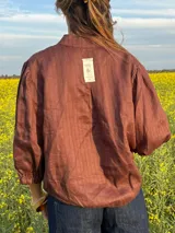 Camisa de lino color marrón oscuro con textura a rayas sutiles, cuello mao, cierre frontal con botones y mangas abullonadas tres cuartos.