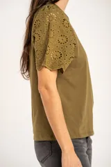 Remera de algodón peinado color negro, con mangas cortas de broderie con diseño calado y terminación festoneada. Presenta un corte oversize y cuello redondo.