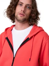 Campera con capucha Caterpillar de color coral, con cierre frontal de cremallera metálica, bolsillos tipo canguro, capucha forrada y puños y bajo de punto acanalado. Cuenta con una pequeña etiqueta con el logo de la marca en el bajo.