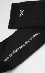 Medias negras de algodón, estilo 3/4, con puño acanalado. Presentan un bordado blanco en la parte superior que simula unas tijeras cruzadas y texto en la planta que dice "Ropa sin género para seres humanos".