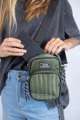 Bandolera porta celular color verde militar, con correa de cinta negra regulable. Presenta un bolsillo frontal con cierre y diseño acolchado con pespuntes verticales.