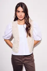 Chaleco sin mangas, color beige claro, con bordados florales en relieve y ribetes a contraste.