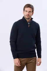 Buzo tejido de punto color verde oscuro, con cuello alto y cierre frontal parcial. Presenta un detalle en cuero en el tirador del cierre y un pequeño logo bordado en el pecho.