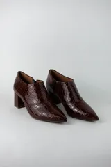 Botines de caña baja con acabado acharolado y textura efecto cocodrilo. Presentan punta fina, cierre lateral y taco cuadrado de altura media.