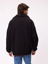 Campera reversible con capucha oculta, confeccionada en sarga de algodón con elastano en el exterior y nylon de poliéster en el interior. Presenta cierre frontal con botones a presión, costuras visibles en contraste y puños elásticos.