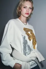Sudadera de cuello redondo y manga larga, con diseño de estampado artístico metalizado en tonos dorados y plateados en el frente. Presenta acabados en rib en cuello, puños y ruedo.
