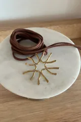 Collar artesanal con dije de forma circular y orgánica, tipo sol, realizado en bronce y alpaca. Incluye un cordón largo de gamuza en color marrón.