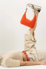 Cartera tipo shoulder bag tejida a mano con punto crochet en raffia color naranja. Tiene asa de cuero marrón y cierre superior con cremallera.