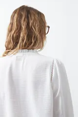 Camisa negra de corte clásico con escote en V, botones frontales y mangas largas con puños. Presenta detalles de recortes calados en la zona de los hombros.