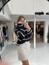 Buzo de tejido de punto grueso en color gris con rayas horizontales en color crema, de corte holgado, cuello redondo y mangas largas.