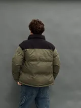 Campera puffer con capucha, diseño bicolor en verde oliva y negro, cierre frontal y bolsillos laterales.