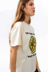 Remera de punto suave de algodón, color beige, con hombros ligeramente caídos y cuello redondo ribeteado acanalado. Cuenta con estampa frontal de la banda The Stone Roses con ilustración de un limón y texto.