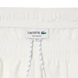 Pantalón de jogging blanco de corte recto con cintura elástica y cordón ajustable. Presenta una franja azul a lo largo de la pierna y el logo de Lacoste bordado en el muslo.
