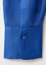 Camisa de ramio color azul eléctrico, de corte recto y largo, con cuello camisero, manga larga con puños abotonados, dos bolsillos de parche en el pecho y cierre frontal con botones.
