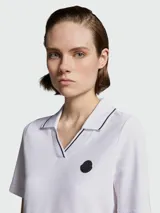 Remera polo de algodón blanca con cuello en V y detalles de líneas finas en contraste. Presenta mangas cortas y el logo de la marca aplicado en el pecho.