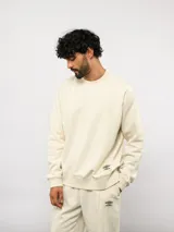 Buzo de felpa color crema, con cuello redondo, manga larga tipo raglán y puños y dobladillo acanalados. Incluye una etiqueta con el logo de Umbro en la parte delantera.