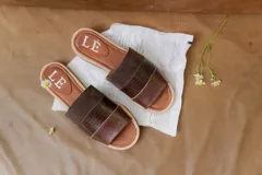 Sandalias planas de cuero marrón con tira ancha sobre el empeine. La plantilla es de cuero con la inscripción "LE".