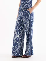 Pantalón azul con estampado de cadenas blancas en piqué de algodón elastizado, de tiro alto y botamanga amplia, con tiras laterales, bolsillos y tajos.