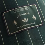 Camiseta de punto oversized verde oscuro de la colección Icons de Adidas, inspirada en los años 80, con rayas diplomáticas blancas, las icónicas tres tiras de la marca en las mangas, cuello redondo y el logotipo del trébol bordado junto al escudo vintage de la Juventus.