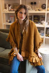 Ruana de punto color mostaza con textura marcada, cuello con volados y lazo regulable. Presenta terminaciones con volados aplicados en lino y flecos en el ruedo, con un diseño amplio y fluido.
