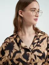 Camisa de manga larga con estampado abstracto en tonos beige y negro, con botones delanteros y bolsillos en el pecho.