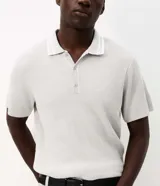 Remera polo marrón de tejido de tricot texturizado, de manga corta, con cuello polo abotonado y detalles de rayas blancas en el cuello.