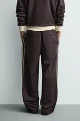Pantalón jogger de corte wide fit en tejido compacto color gris oscuro. Presenta cintura elástica con cordón ajustable, bandas laterales en contraste color beige y costuras frontales tipo pinza.