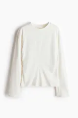 Top de manga larga confeccionado en punto de algodón, con cuello redondo, hombros caídos y detalle de frunces laterales que crean un efecto drapeado, finalizando en un bajo acampanado.