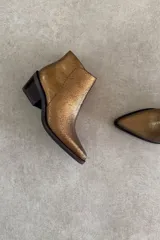 Botín Indiana de cuero vacuno con acabado metalizado dorado, diseño de caña baja, taco cuadrado y punta fina.