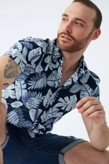 Camisa de manga corta con estampado botánico de hojas en tonos azul y blanco. Presenta cuello clásico, cierre frontal abotonado y corte slim.
