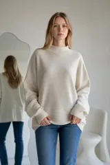Sweater de punto color crema, con cuello alto y diseño holgado. Presenta puños y ruedo acanalados con detalle de líneas horizontales en la parte inferior.