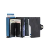 Billetera compacta de cuero genuino color azul con costuras en contraste. Posee un tarjetero de aluminio con sistema de deslizamiento, protección RFID y compartimento para billetes. Presenta cierre lateral con broche a presión y logo grabado.