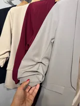 Blazer de corte sastre en color gris claro, con solapas clásicas, bolsillos frontales con solapa y mangas con detalle de frunce.