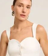 Blusa de sastrería color blanco, sin mangas, con escote corazón, breteles anchos y cierre frontal con botones forrados. Presenta un dobladillo en punta y espalda elástica.