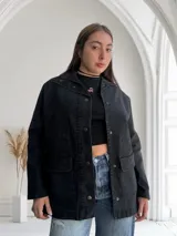 Sobrecamisa negra de jean con cuello camisero, cierre frontal con botones metálicos, bolsillos de parche en el pecho y corte recto.