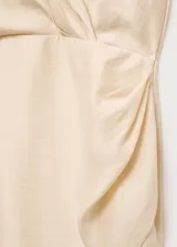 Vestido corto color crema, con escote en V cruzado, sin mangas y falda cruzada con drapeado lateral.