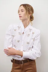 Camisa blanca de manga corta con cuello mao y volados, botones frontales y bordados de hojas y flores en color dorado.