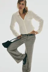 Pantalón sastrero de tiro alto con piernas amplias y pliegues frontales. Presenta un estampado de cuadros Príncipe de Gales en tonos grises, beige y negro.