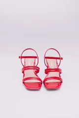 Sandalias de tacón cuadrado medio, confeccionadas en charol rojo. Presentan un diseño de tiras tubulares sobre el empeine y cierre con pulsera ajustable al tobillo mediante hebilla metálica.