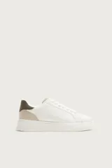 Zapatilla deportiva de diseño minimalista con parte superior lisa, suela con volumen y detalle de color a contraste en el talón.
