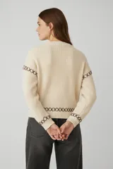Sweater de tejido de punto grueso color gris oscuro, con cuello redondo a la base y mangas largas. Presenta detalles de bordado decorativo en color blanco con diseño de cruces en las mangas y el ruedo.