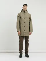 Gabardina con capucha de corte recto y largo medio. Cuenta con cierre frontal engomado, cartera con botones a presión, bolsillos laterales y tejido repelente al agua y al viento.