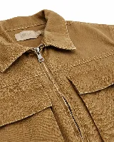 Chaqueta de twill color tostado con cierre frontal, cuello camisero y bolsillos frontales con solapa. Presenta costuras reforzadas visibles y un diseño de estilo utilitario.