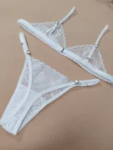 Conjunto de lencería de dos piezas confeccionado en encaje blanco con diseño floral. Incluye un sostén triangular con tirantes regulables y una bombacha colaless ajustable con tiras laterales.