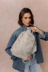 Mochila compacta de color beige, con compartimento principal con cierre, bolsillos laterales y bolsillo frontal con cierre oculto. Cuenta con correas regulables y acolchonadas y asa superior.