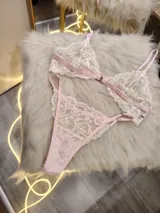 Conjunto de lencería compuesto por un bralette y una tanga, confeccionados en encaje bitono rosa y champagne con diseño floral. El bralette presenta cierre frontal con broche de gancho y breteles regulables. La tanga es de estilo colaless con laterales regulables.