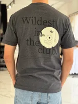 Remera gris melange de manga corta y corte clásico, con estampa en la espalda que dice "Wildest in the club" junto a un gráfico de un disco compacto.
