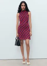 Vestido corto sin mangas con cuello alto, confeccionado en tejido estampado con patrón geométrico en tonos rojos y violetas.
