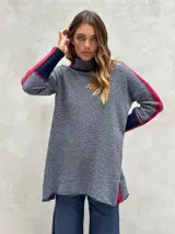 Sweater de punto con patrón de espiga en tonos beige y marrón, cuello alto, mangas largas con detalles en naranja y puños marrones.