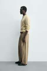 Pantalón chino de corte wide fit confeccionado en tejido de algodón. Presenta pliegues frontales, bolsillos laterales y bolsillos traseros de vivo, con cierre frontal de cremallera y botón.